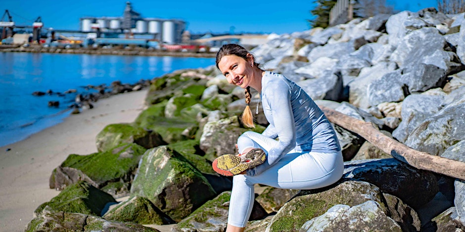 fit woman stretching her glutes while sitting on a rock at the beach